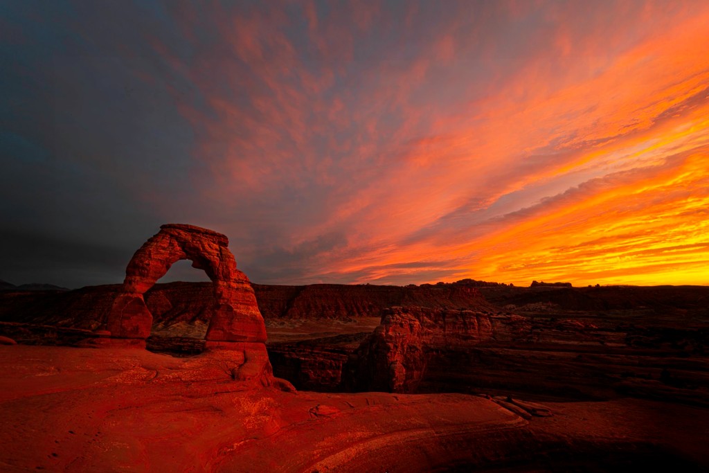 Sunset casting a warm red glow over Delicate Arch in the desert landscape.